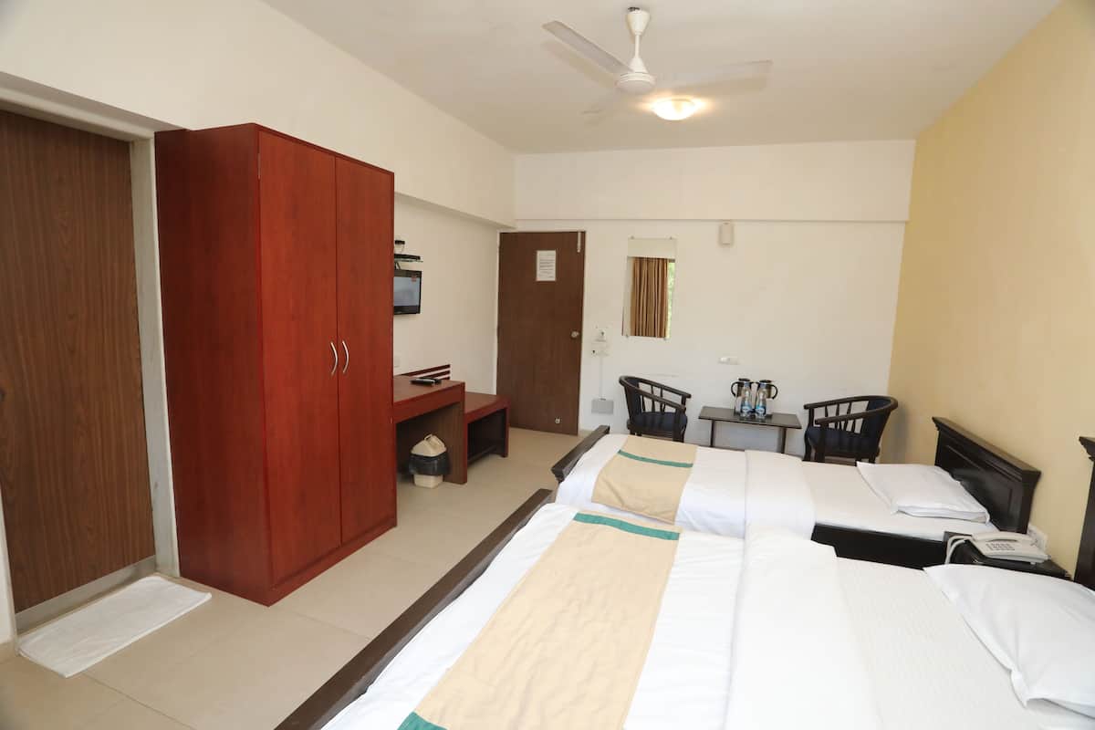 A hotel room with two beds, a wardrobe, a desk with a chair, a small table with two chairs, and a ceiling fan.