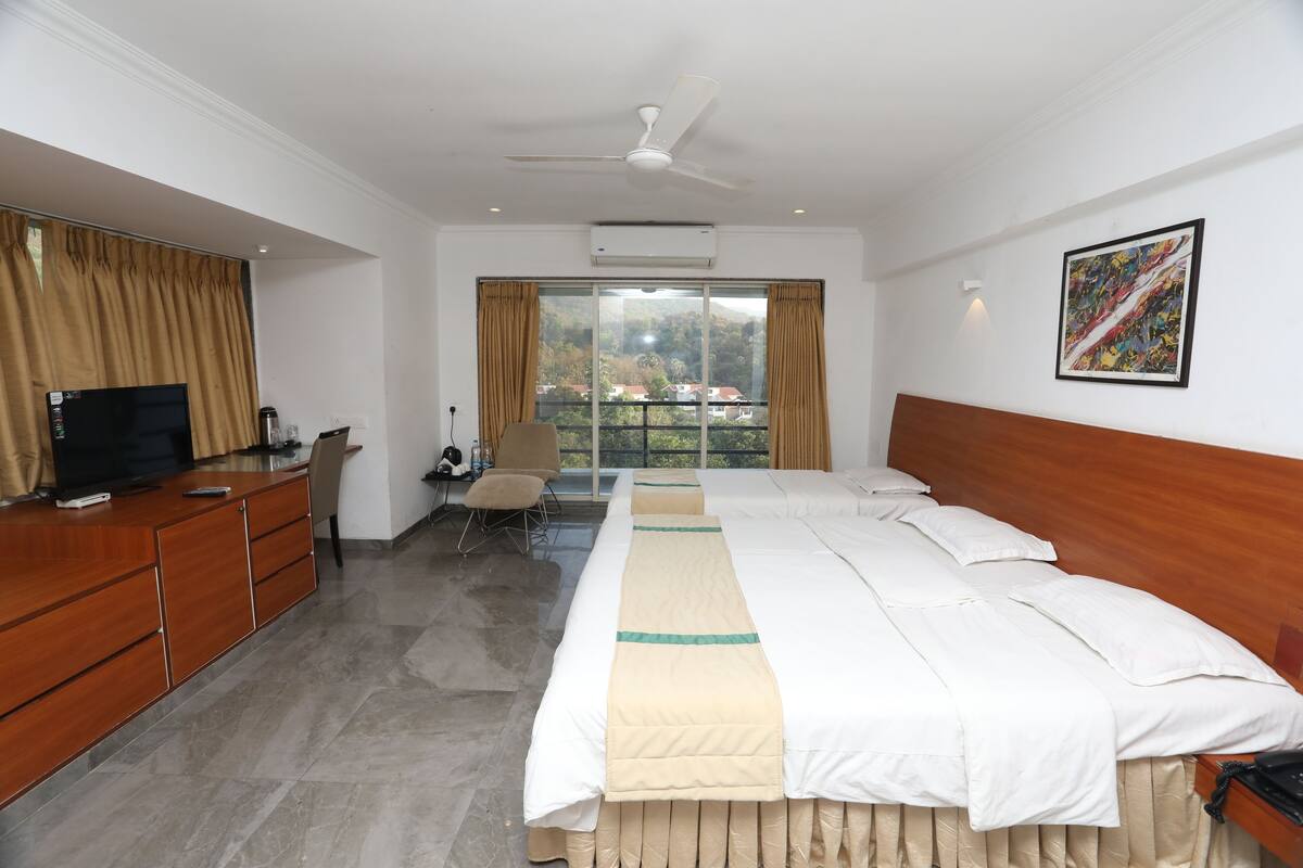 A hotel room with a bed, a desk with a TV, a chair, and a view of the outside.