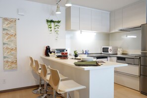 Una cocina moderna con una isla central, taburetes de bar, electrodomésticos de acero inoxidable y una planta colgante.