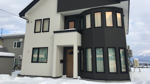 A two-story house with a white and dark brown exterior, multiple windows, and a snow-covered roof. - Jadan House (Furano)