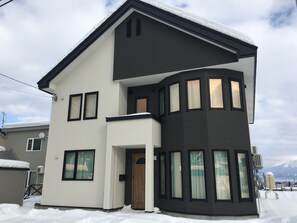 A two-story house with a white and dark brown exterior, multiple windows, and a snow-covered roof.