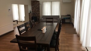 A spacious living area with a long wooden dining table, comfortable seating, a fireplace, and large windows with curtains. - Jadan House (Furano)