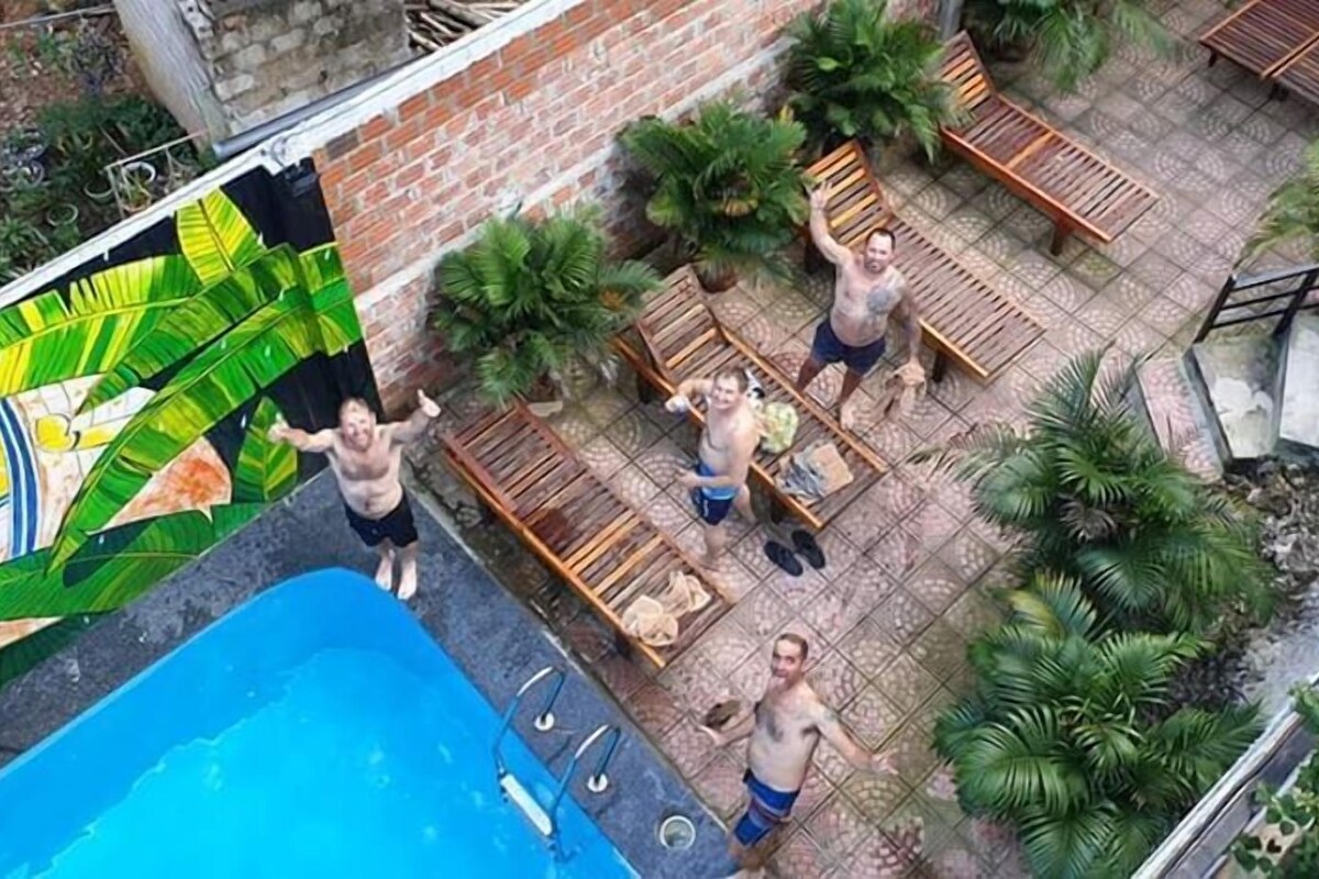 Un área de piscina en la azotea con piscina azul, sillones de madera y plantas en macetas.