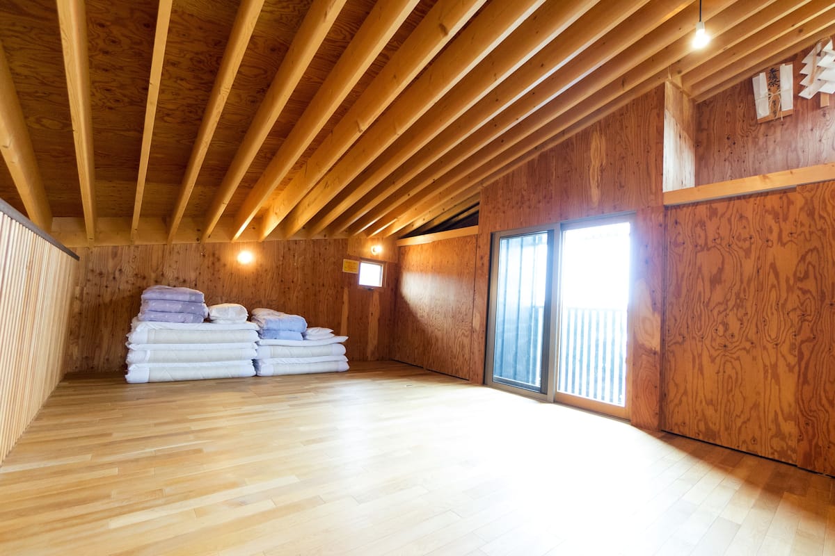 Una habitación con vigas de madera en el techo, una pila de toallas y un ventanal grande.