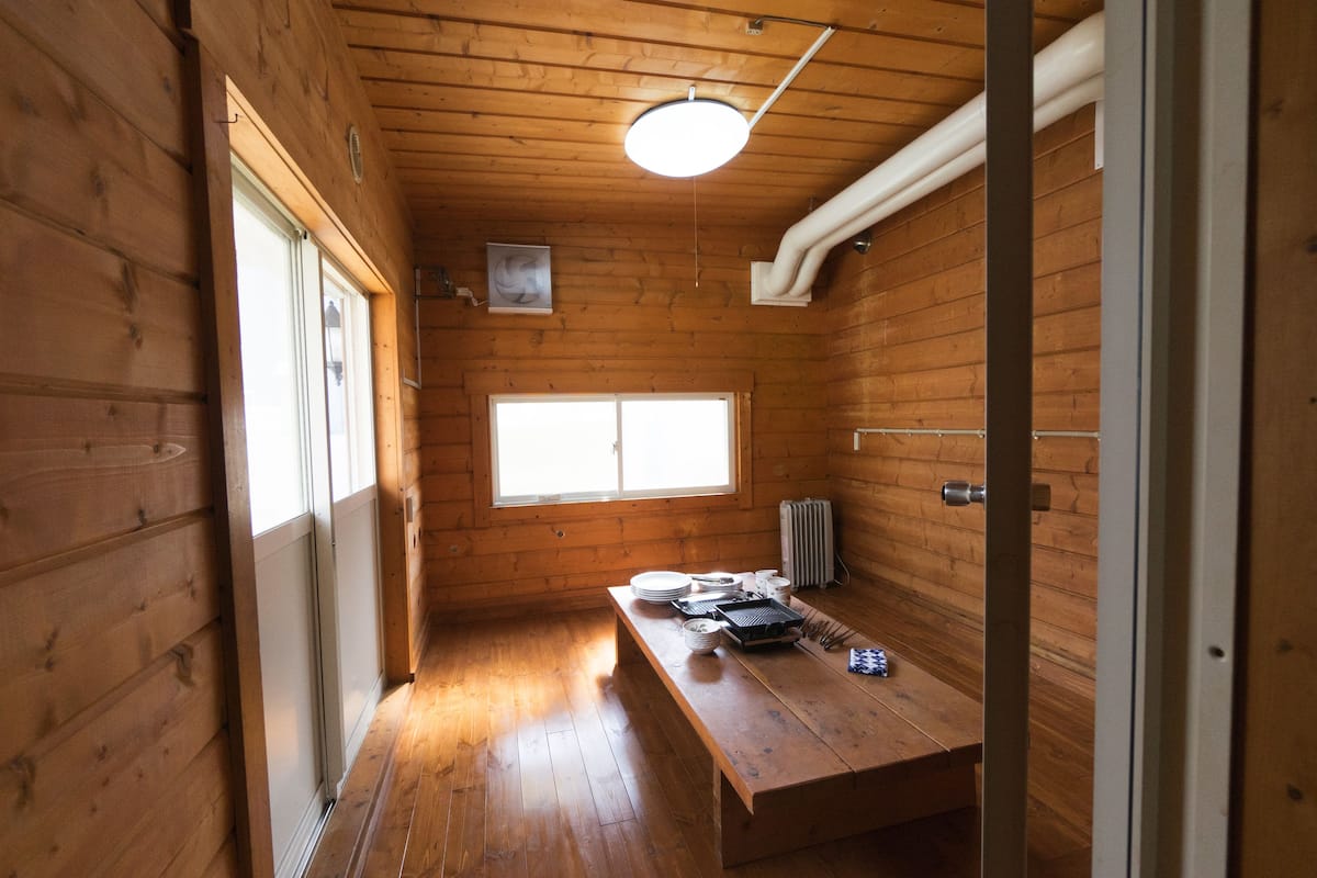 Un estrecho pasillo de madera con suelo de madera, una ventana y una mesa con platos y una tetera.