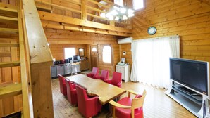 Ein Interieur einer Holzhütte mit Esstisch, roten Stühlen, einem Fernseher und einer Küchenzeile.