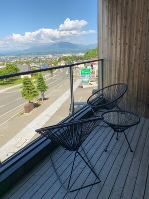 A balcony with two black wire chairs, a wooden floor, and a view of a road with a sign for 'Kitchen Farm F's gate'.