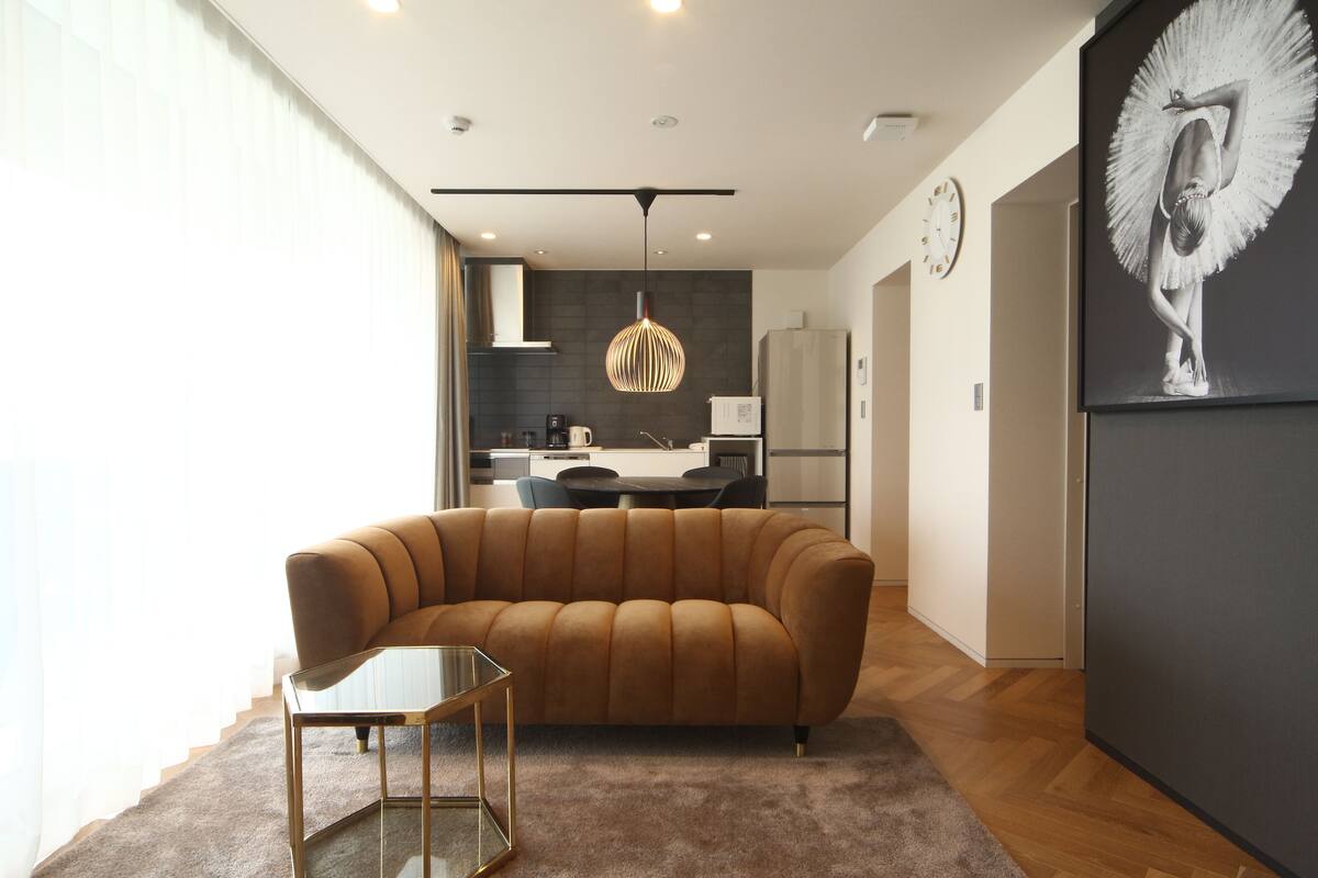 A modern living room with a brown sofa, a glass coffee table, and a dining area in the background.