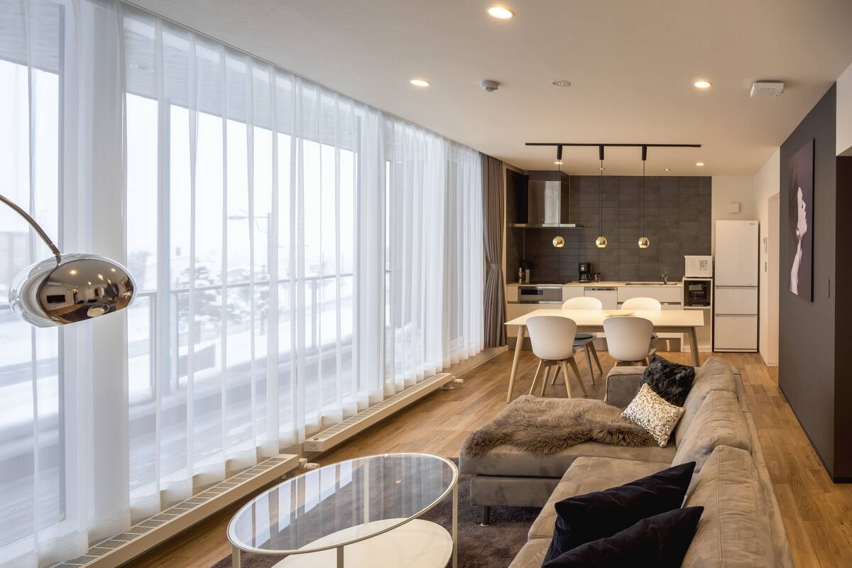 A modern living room with a sofa, a glass coffee table, and a dining area with a white table and chairs.