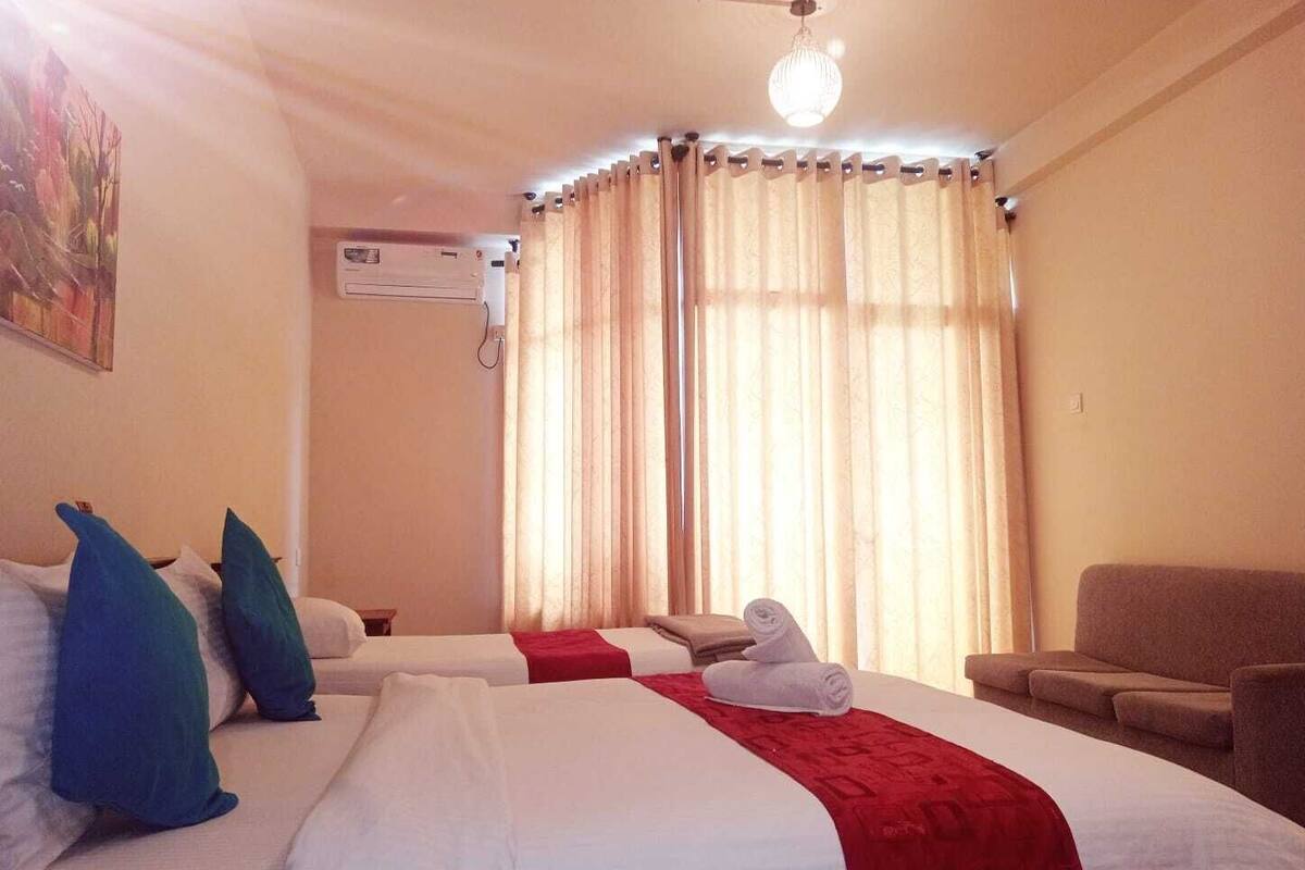 A hotel room with two beds, a red blanket, a white towel, a ceiling fan, and a large window with curtains.