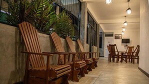 A row of wooden chairs and a dining table in a well-lit hallway with a tiled floor and a view of a building outside. - Ella Mansion (Ella)