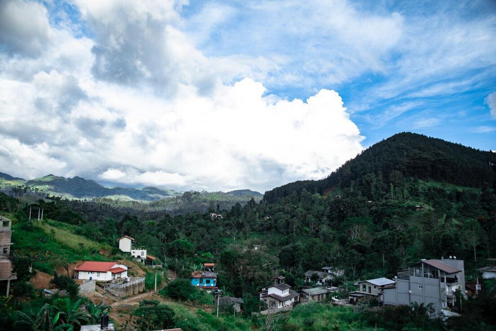 Un village rural où les maisons sont entourées d’une végétation luxuriante et où l’on aperçoit des montagnes au loin.