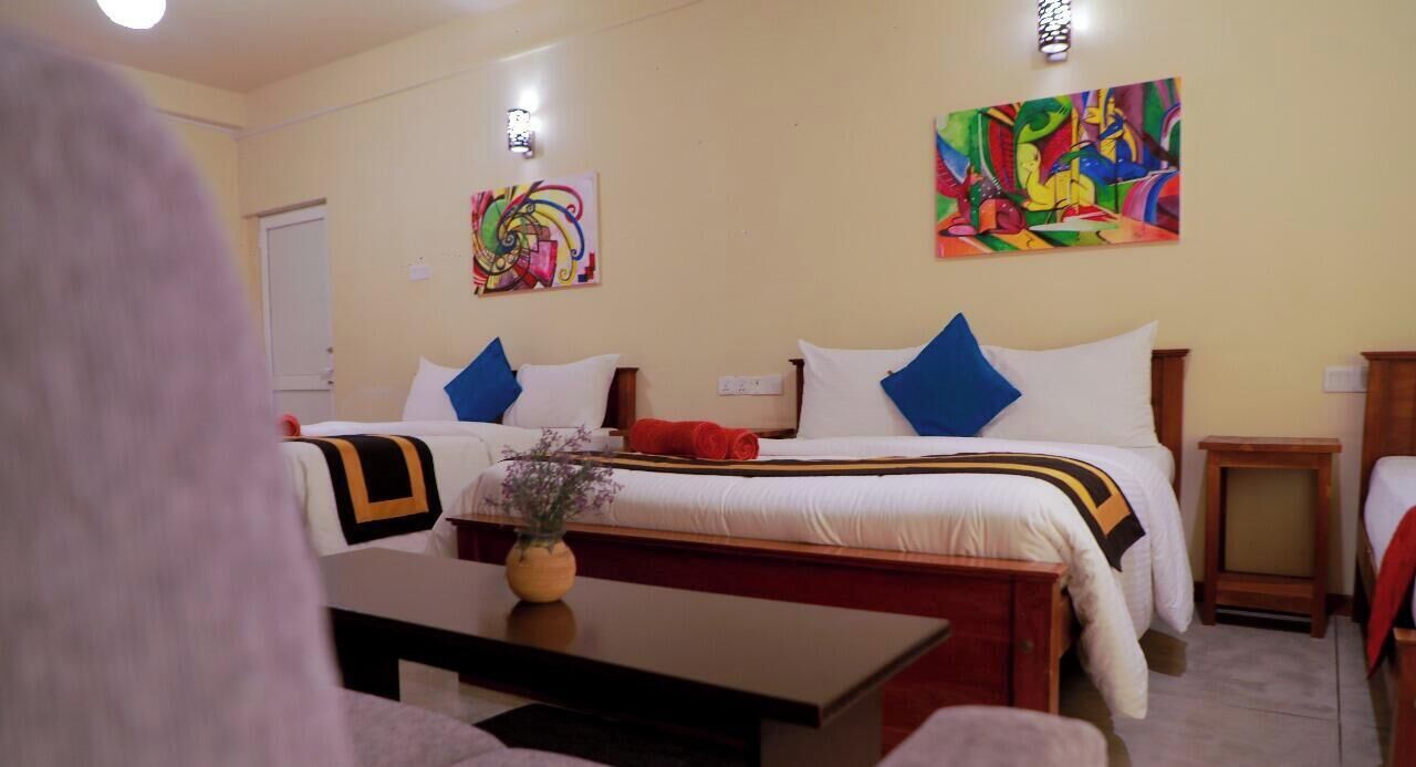 Een hotelkamer met twee bedden, een houten nachtkastje, een tafeltje met een vaas, en kleurrijke abstracte kunst aan de muren.