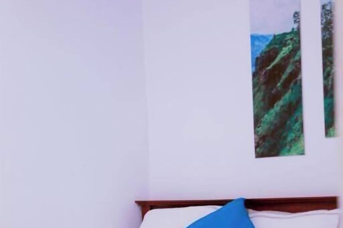 A single bed with white bedding, a blue pillow, and a red blanket. There are rolled towels on the bed.