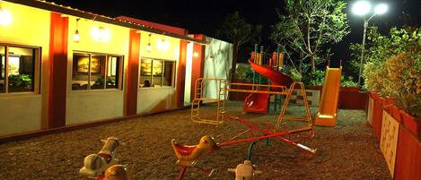 A playground with swings and a slide, surrounded by a building with windows and a door.