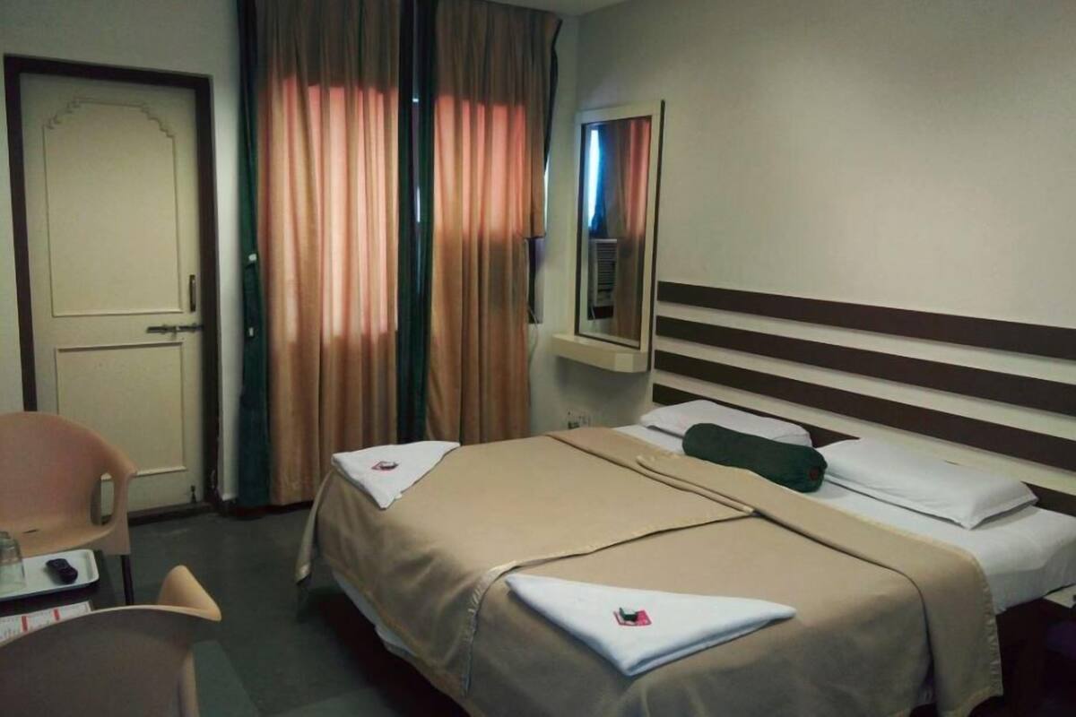 Habitación de hotel con dos camas, un escritorio, una silla y una ventana con cortinas.