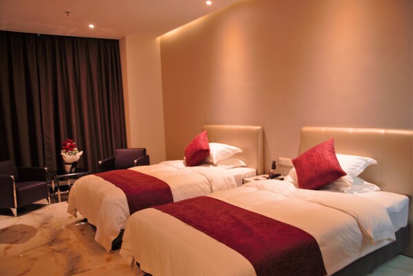 Ein Hotelzimmer mit zwei Betten, jedes mit einem roten Akzentkissen, einem Marmorboden und dunklen Vorhängen im Hintergrund.