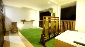 Une pièce avec une moquette verte, une chaise en bois, un paravent en bois orné d’une plante et une grande fenêtre donnant sur le ciel nocturne.