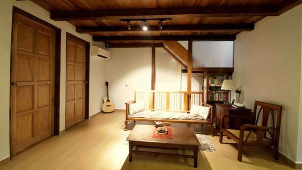 Une pièce chaleureuse avec un plafond en bois, un canapé en bois, une petite table et une guitare appuyée contre le mur.