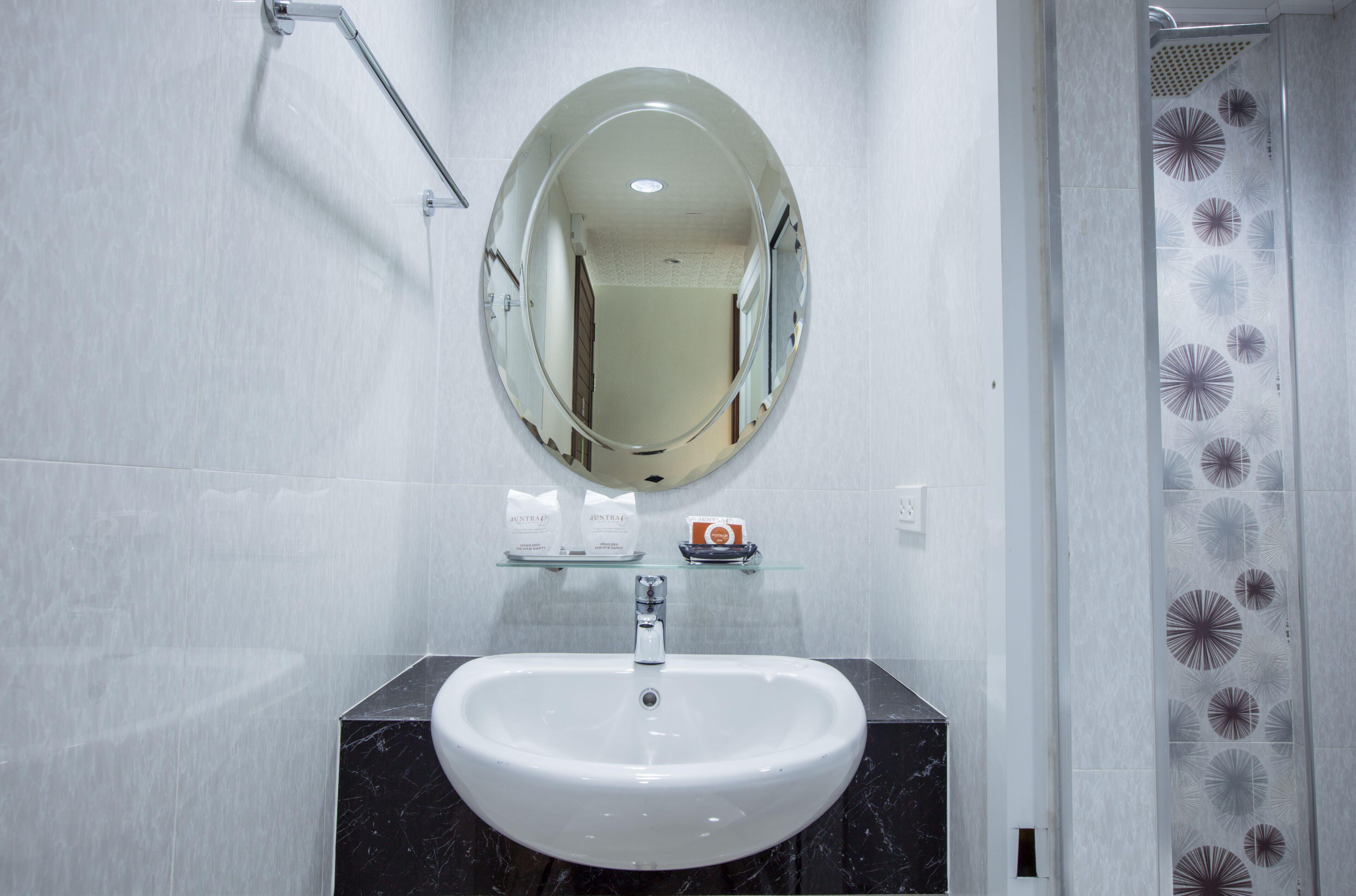 Een badkamer met een wit wastafelmeubel, een spiegel en een glazen plank met toiletartikelen.