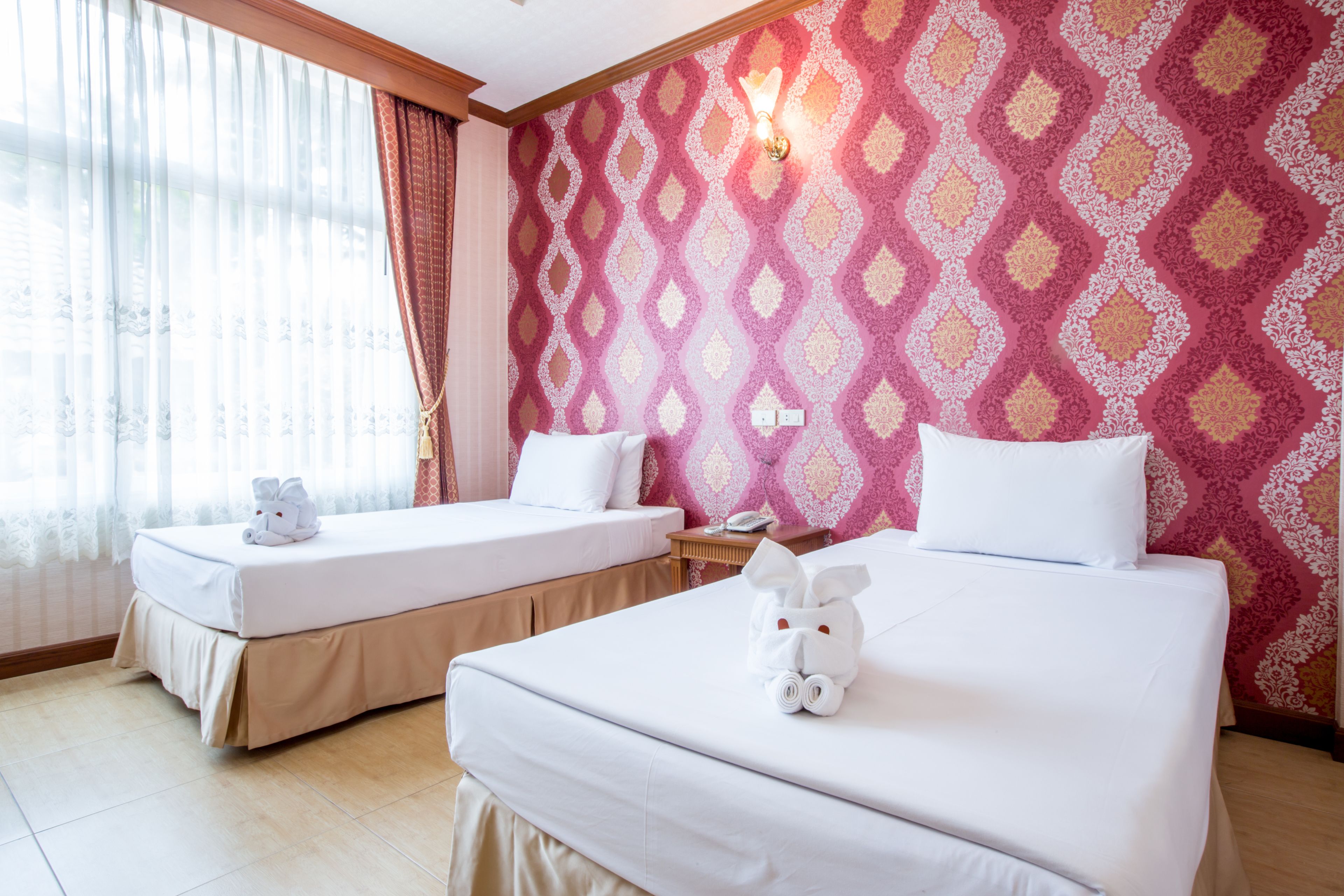 A hotel room with two beds, each with a white comforter and pillows, and a wall with a patterned wallpaper.