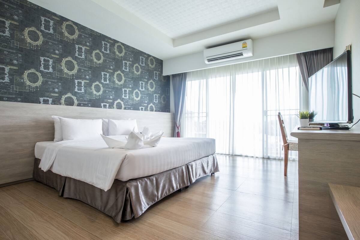 A modern hotel room with a large bed, a desk, and a view of the outdoors.