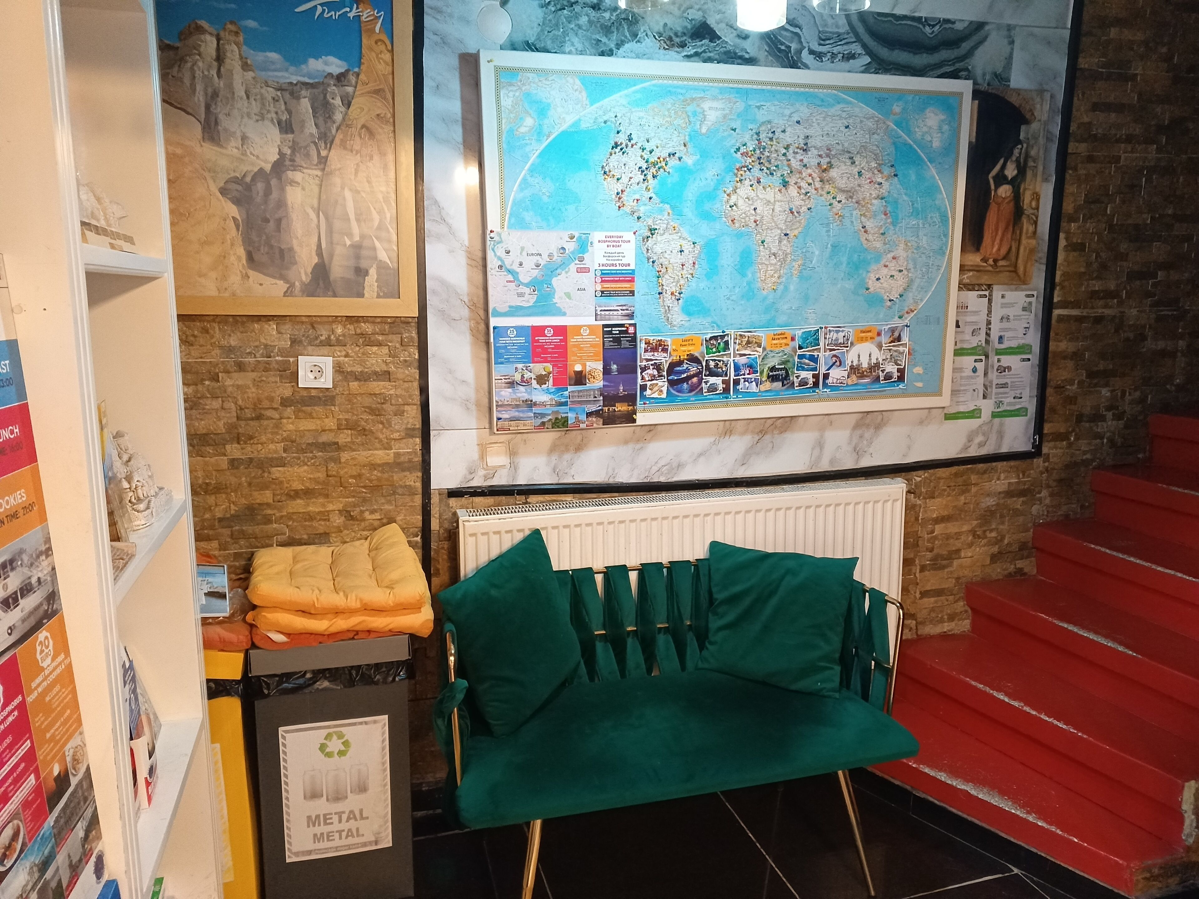 A room with a world map, a radiator, a green chair, a trash bin, and a red staircase.