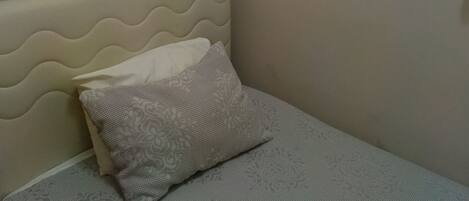 Un dormitorio con cama, almohada, cabecera, ventana con persianas y un cuadro colgado en la pared.