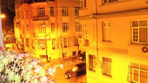 Un edificio de varios pisos con balcones y ventanas, una calle con coches estacionados y una señal de tráfico visible.