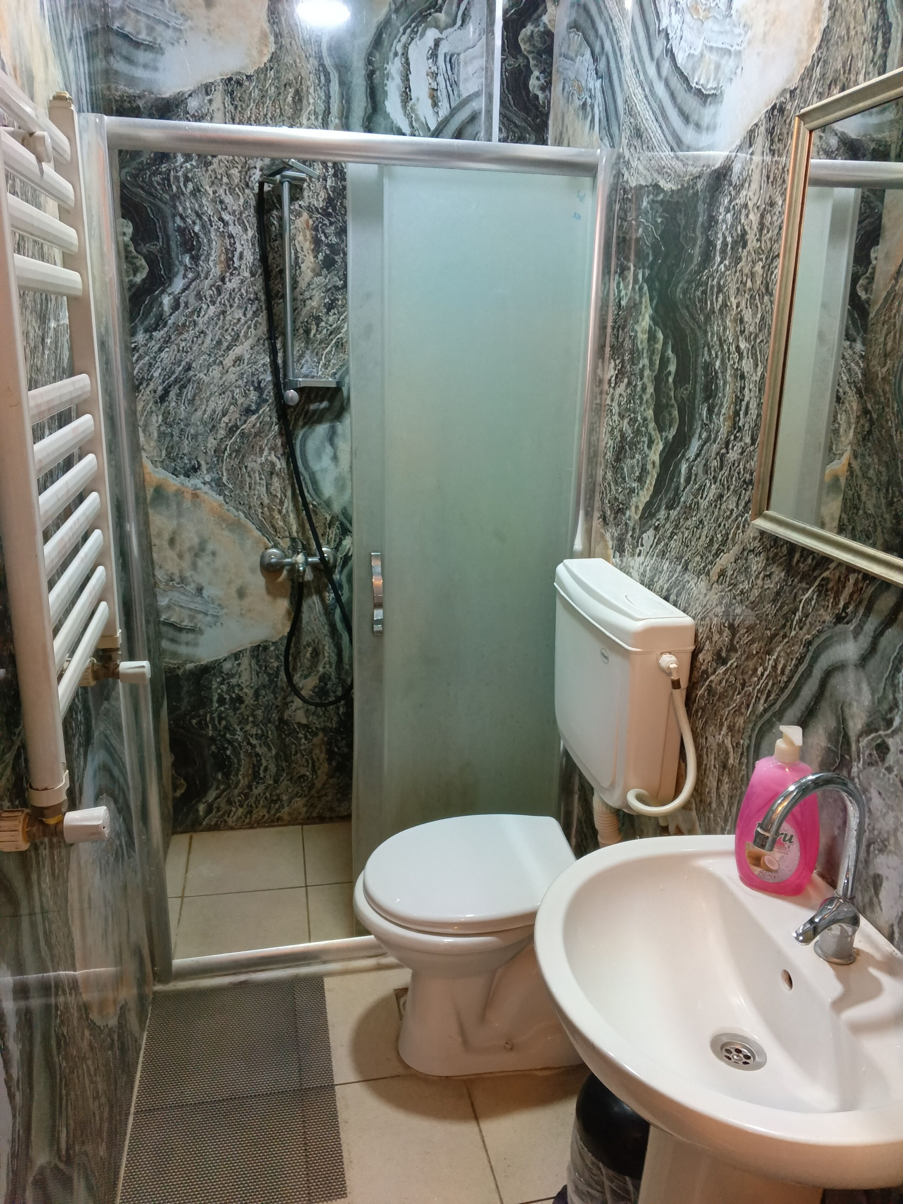 A bathroom with a marble wall, a toilet, a sink, and a shower enclosure.