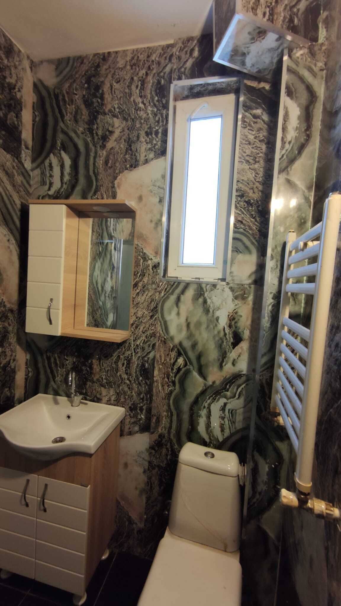 A bathroom with a marble wall, a sink, a toilet, and a window.