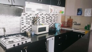 A kitchen with black cabinets, a gas stove, a microwave, and a tiled backsplash. - Avrasya Hostel (Istanbul)