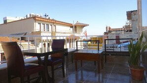 Un balcón con mesa y sillas, una planta en maceta y vistas a edificios.