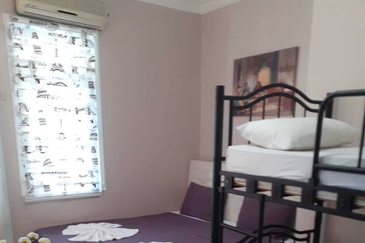 A dormitory room with bunk beds, a small table with a chair, and a window with blinds.