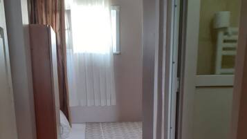 Een smalle gang die leidt naar een slaapkamer met een bed, een raam met gordijnen en een rode vloerkleed.