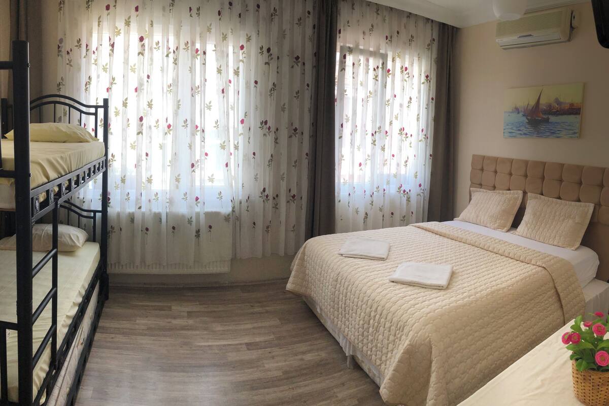 A bedroom with a bunk bed, a single bed, and a window with floral curtains.