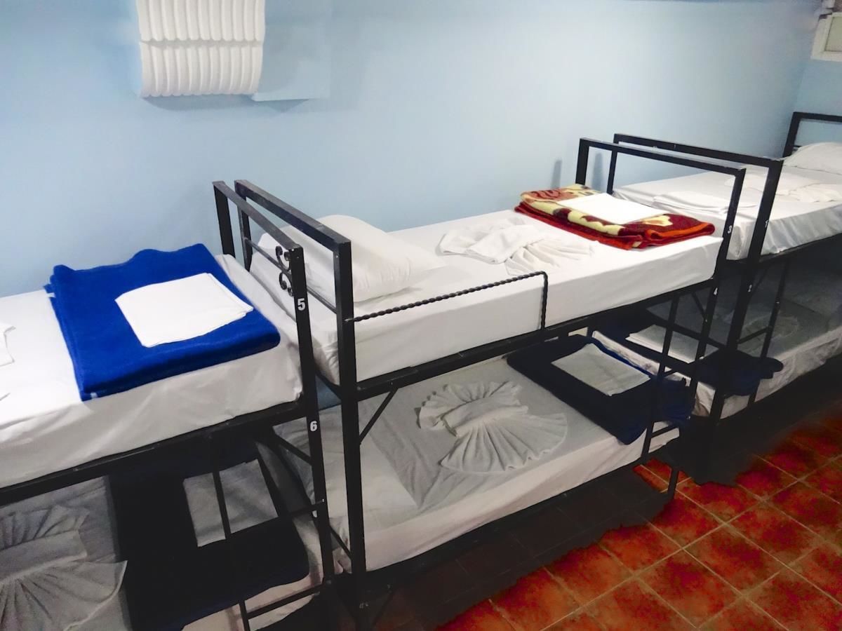 A dormitory room with bunk beds, white bedding, and a blue blanket on one bed.