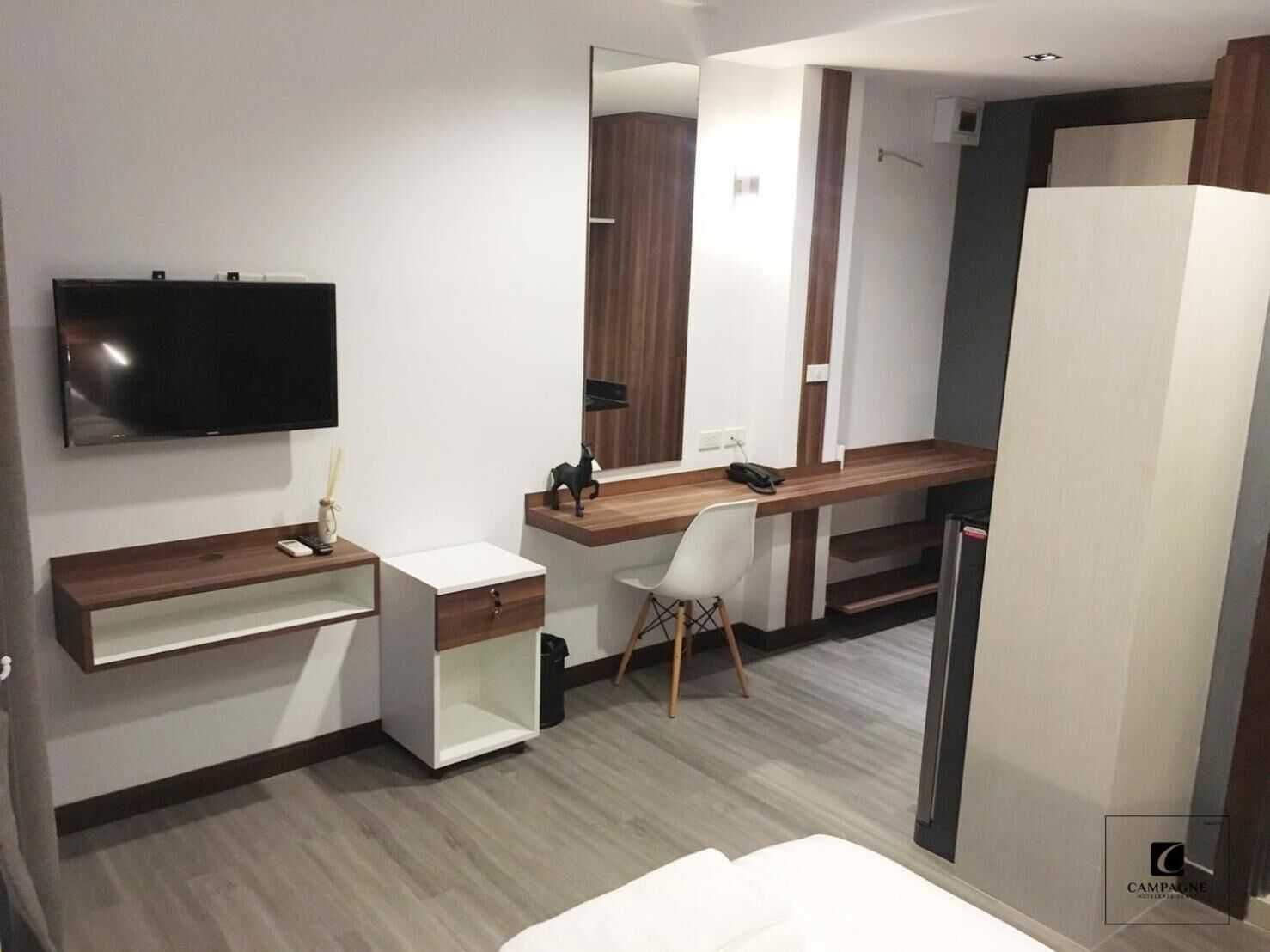 Et moderne hotelværelse med et fladskærms-tv, et træskrivebord, en hvid stol, et stort spejl og et garderobeskab.