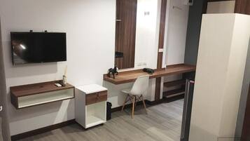 Et moderne hotelværelse med et fladskærms-tv, et træskrivebord, en hvid stol, et stort spejl og et garderobeskab.