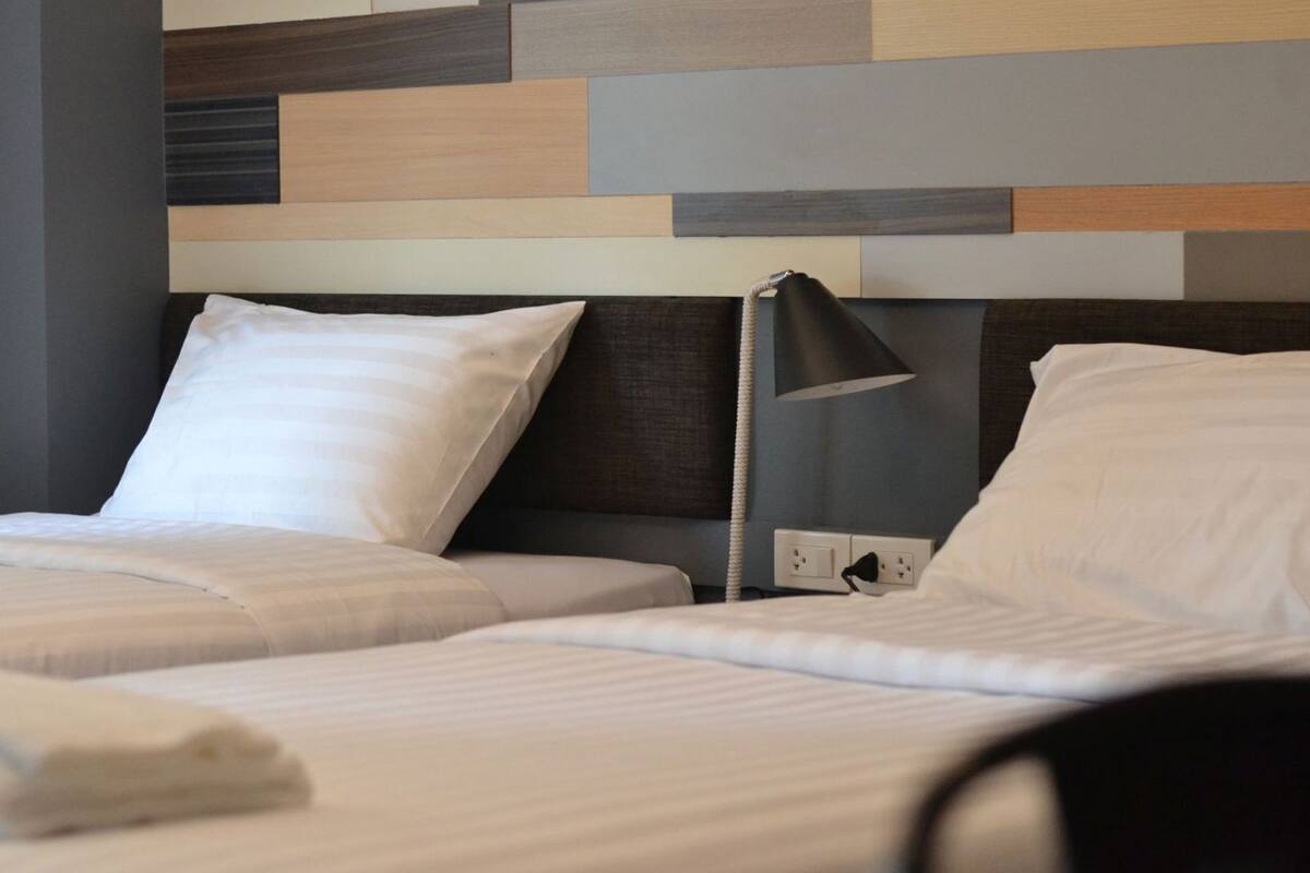 Une chambre d’hôtel avec deux lits, une tête de lit moderne, une lampe de chevet et une prise de courant.