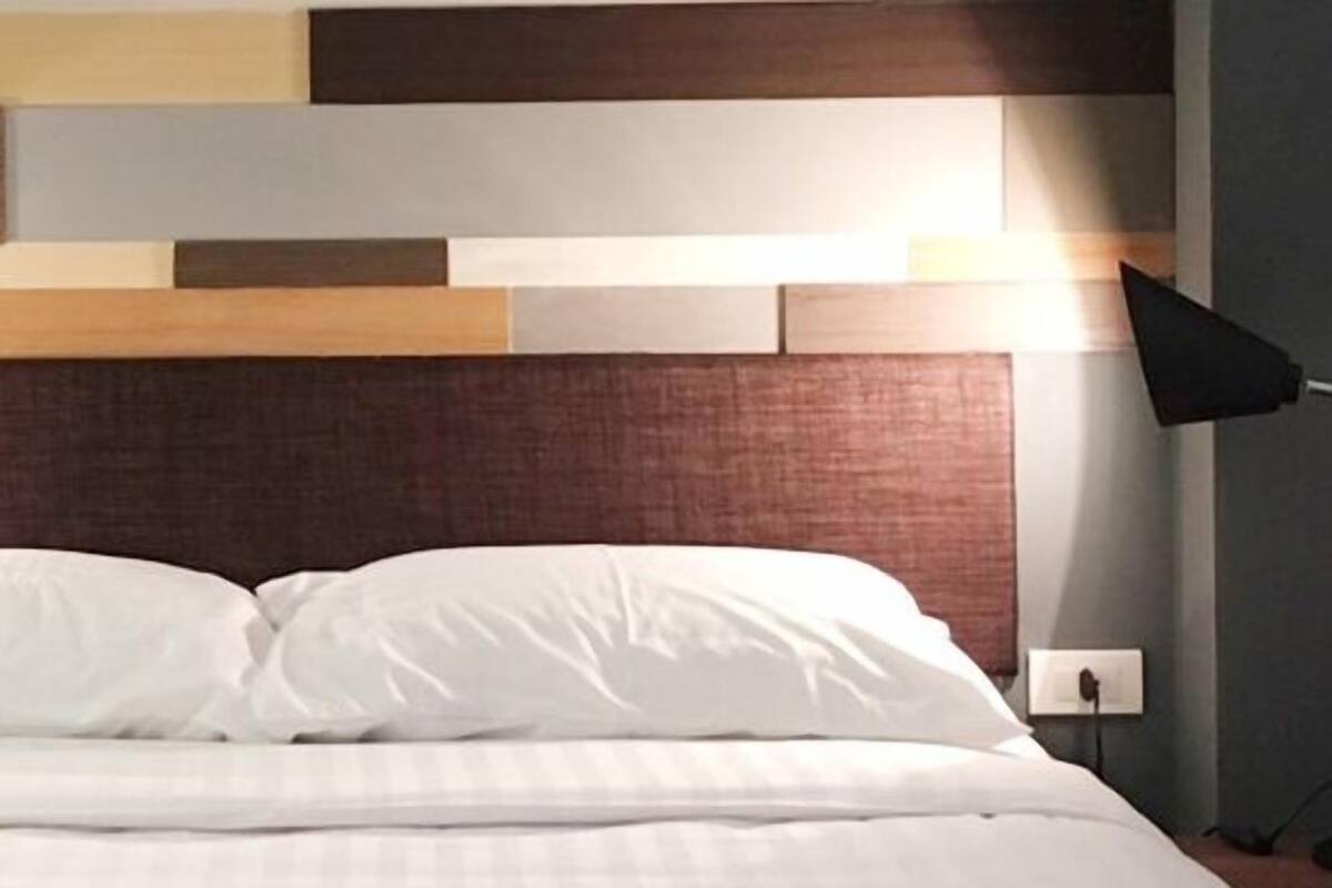 Un lit avec une literie blanche, une tête de lit en bois et une lampe de sol noire.