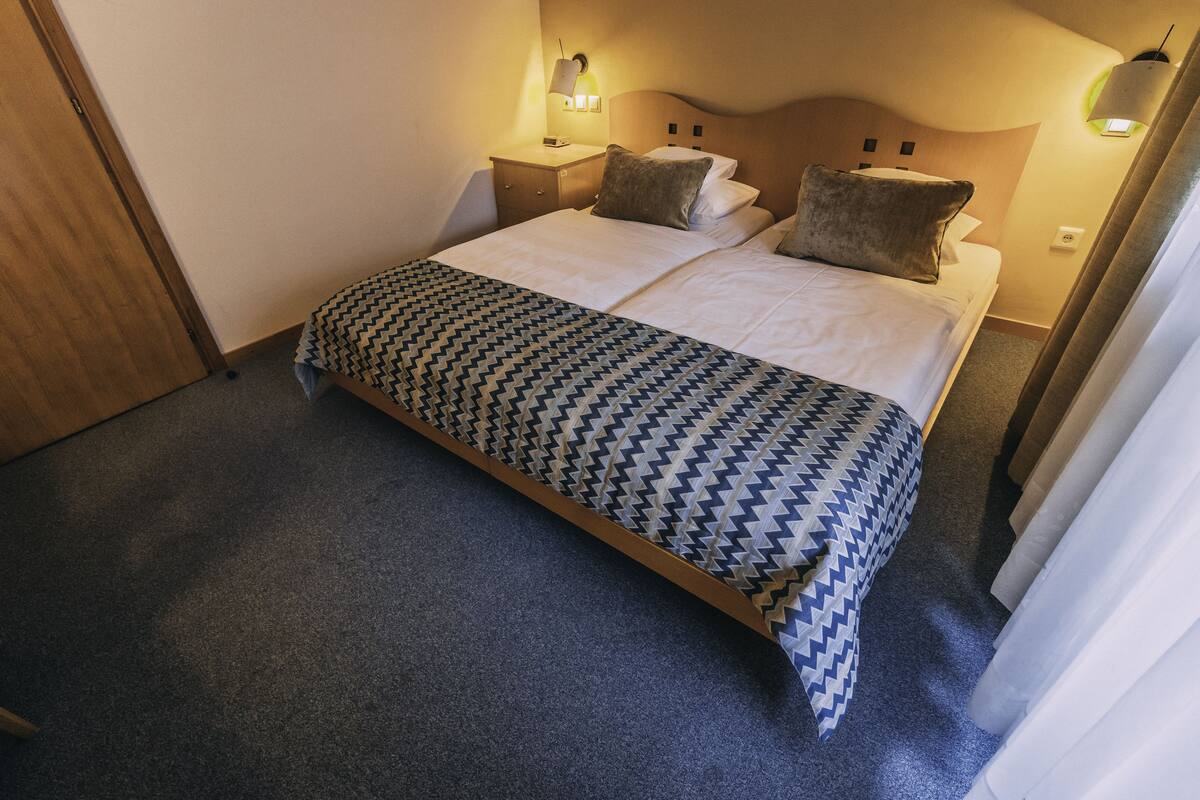 Una habitación de hotel con una cama grande, dos mesitas de noche, una colcha estampada y luces fijadas a la pared.