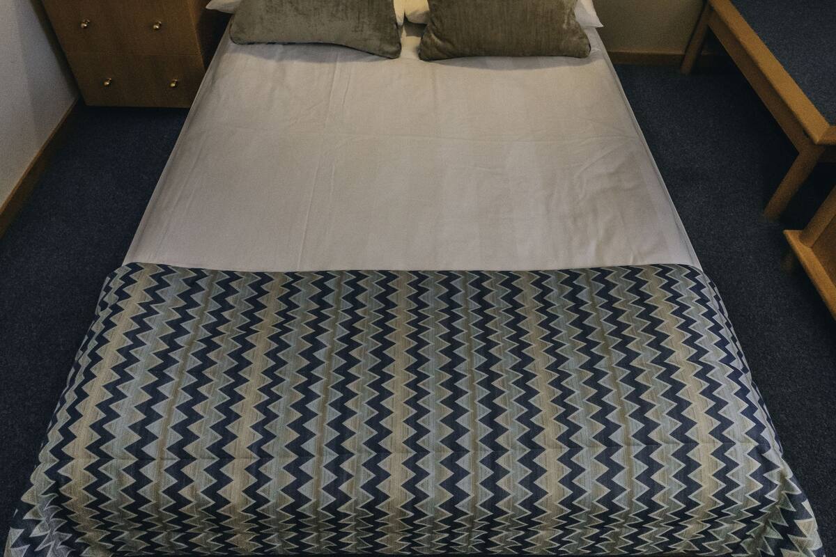 Una cama bien tendida con una colcha estampada, un cabecero de madera y una lámpara de noche.