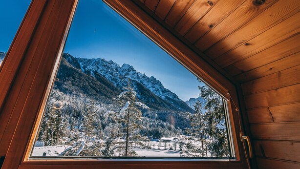 Una baita di legno con un'ampia finestra che si affaccia su un paesaggio montano innevato.