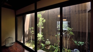 A room with a sliding glass door leading to a garden with a wooden fence, a stone lantern, and a birdcage. - Inari Ohan (Kyoto)