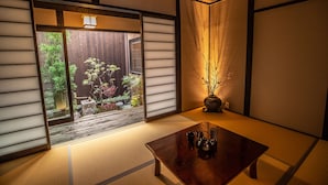 A traditional Japanese room with tatami flooring, a sliding door leading to a garden, and a wooden table with a vase of dried plants. - Inari Ohan (Kyoto)