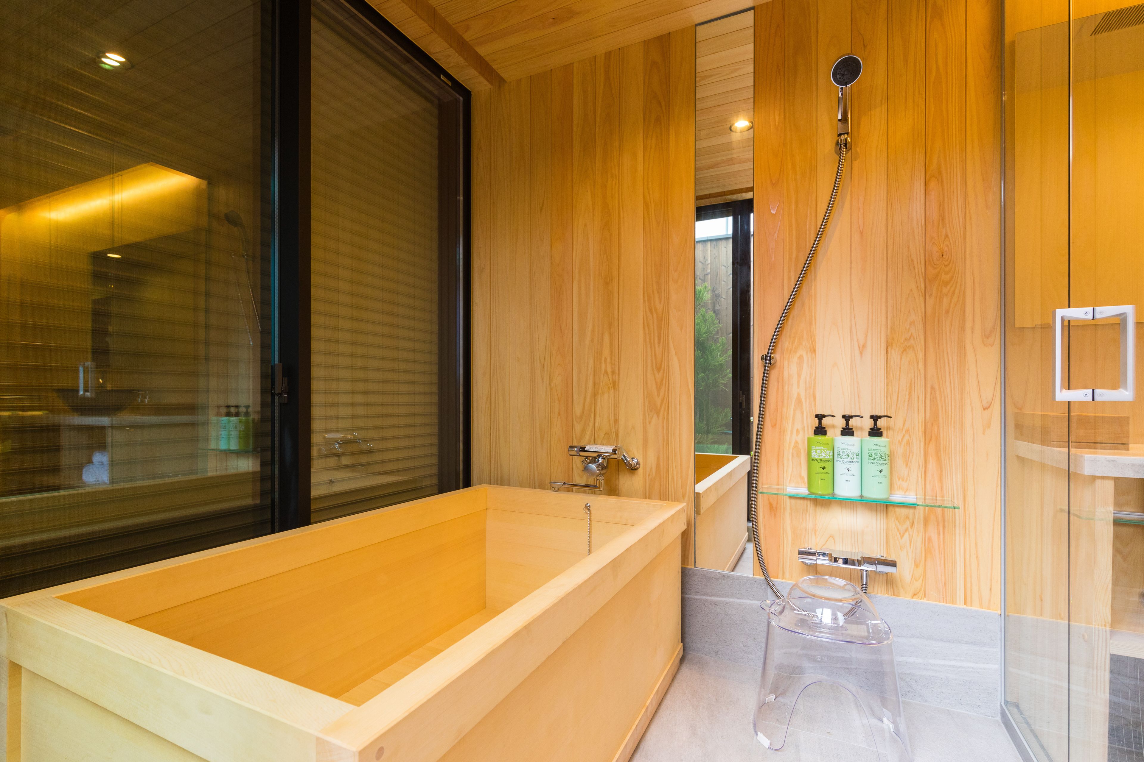 A modern bathroom with a wooden bathtub, glass shower enclosure, and a shelf with toiletries.