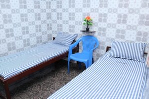 A room with two single beds, a blue plastic chair, and a small table with a potted plant. - SIU Mansion Lodge (Chennai)