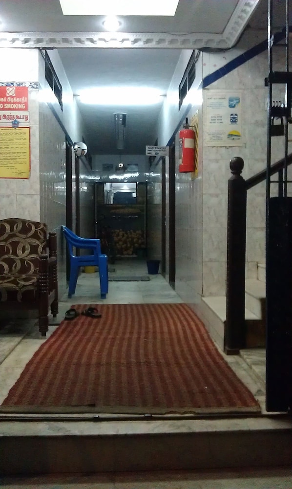 A hotel lobby with a patterned carpet, a blue chair, a wooden chair, and a fire extinguisher. - SIU Mansion Lodge (Chennai)