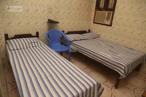 A room with three single beds, a blue chair, a telephone, and an air conditioning unit.
